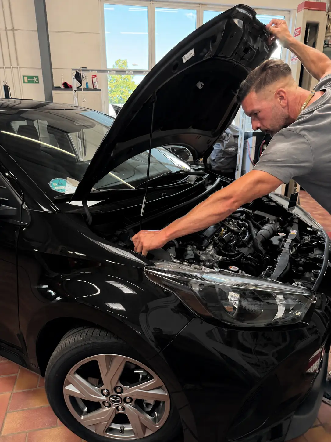 Klimaservice in Magdeburg: Mechaniker öffnet die Motorhaube eines schwarzen Mazda in der Werkstatthalle.