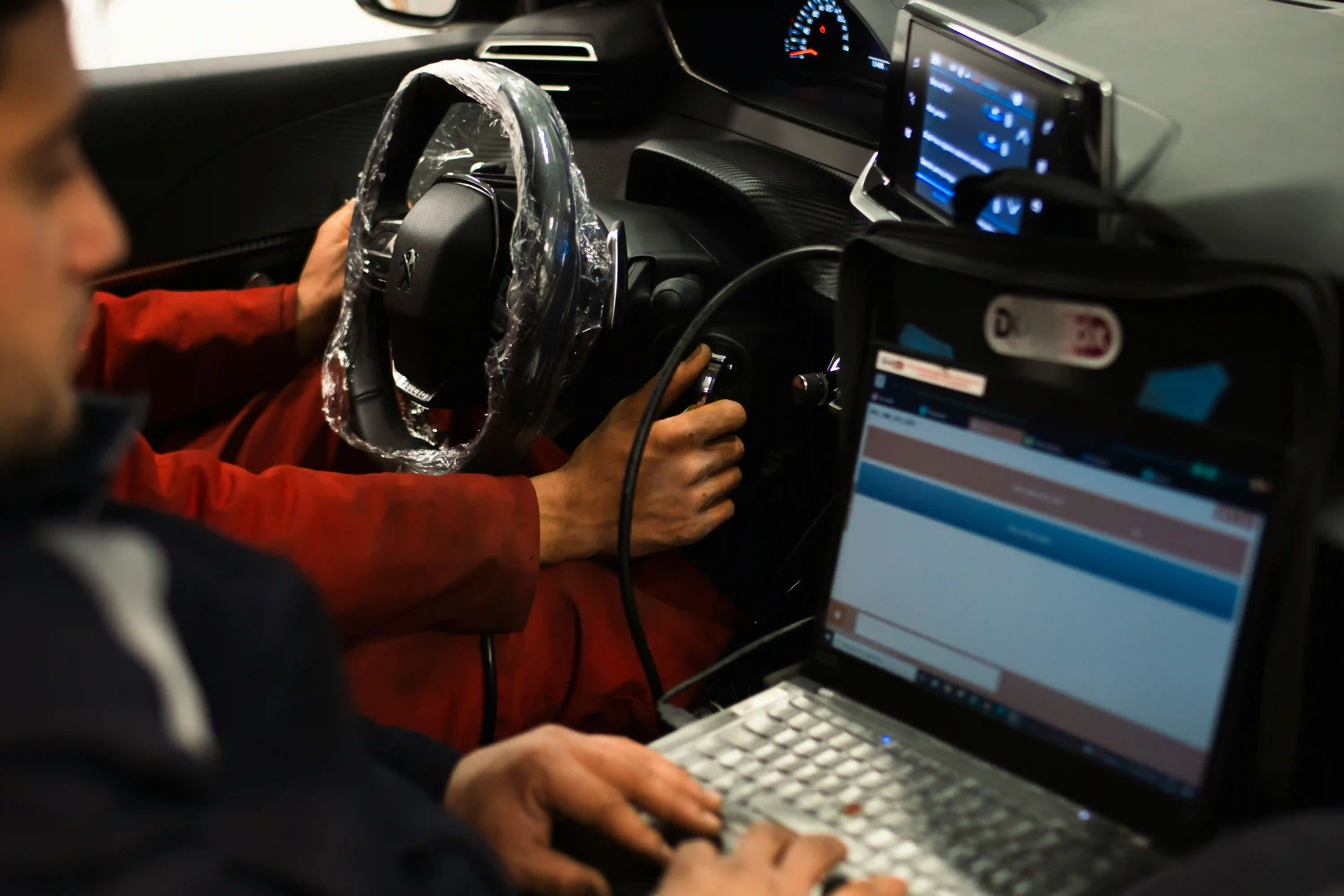 Fehlerspeicher auslesen: ein Diagnosekabel steckt im OBD-Anschluss unter dem Lenkrad, daneben liegt ein Laptop mit der Diagnosesoftware.