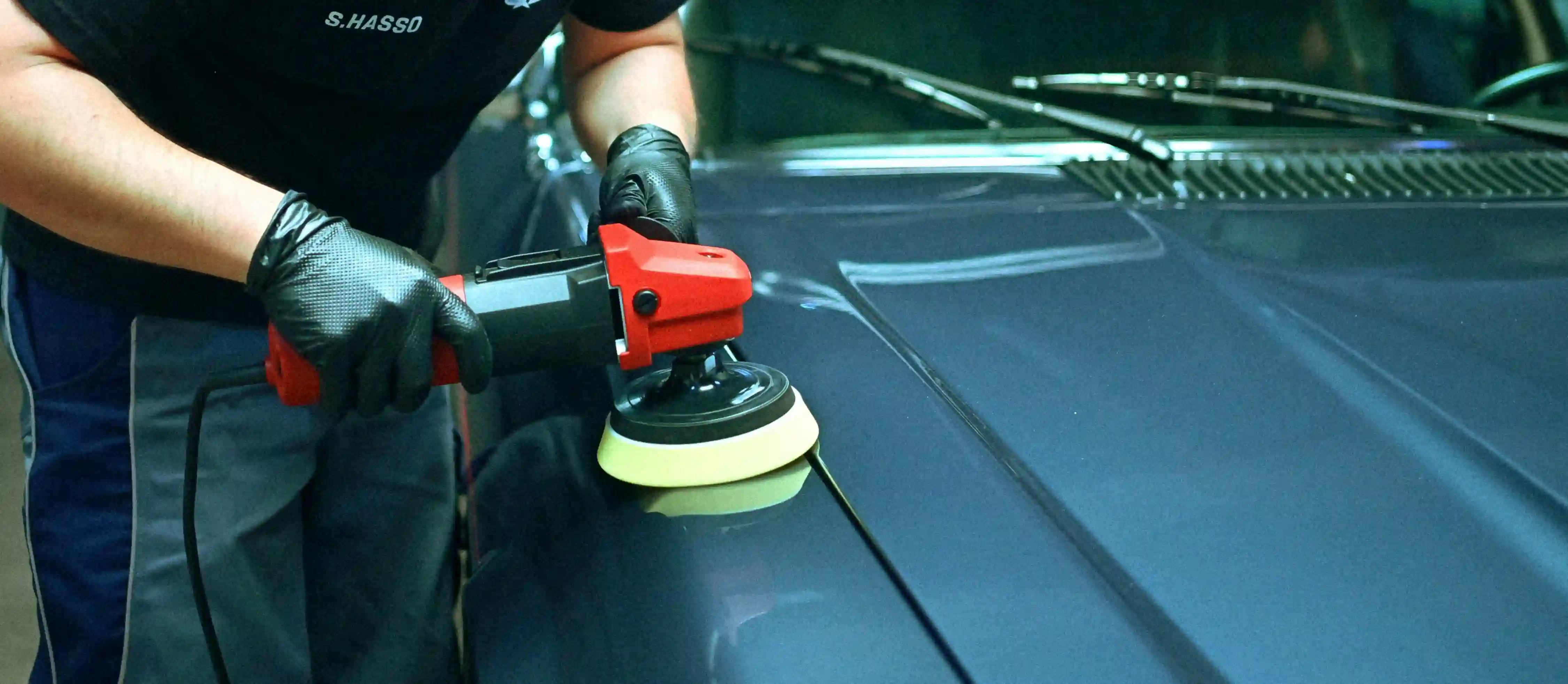 Lack aufbereiten: eine Poliermaschine mit gelbem Schwamm läuft über die dunkelblaue Motorhaube eines Autos.